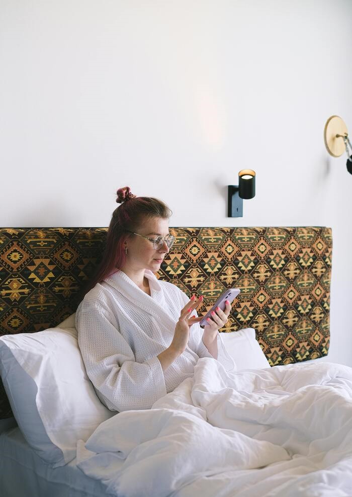 mujer en cama con bata, observando su celular